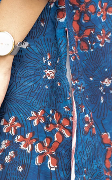 Close-up of a blue patterned garment with red and white floral print, showing part of a person's arm and a watch at the upper left.