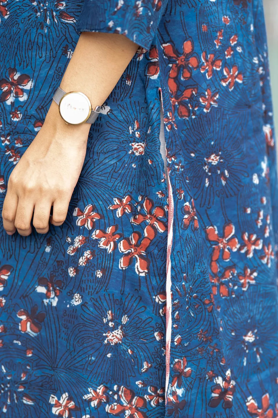 A close-up of a person wearing a blue patterned dress or kurta with red and white floral motifs, along with a silver-toned watch on the wrist.