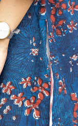Close-up of a blue patterned garment with red and white floral print, showing part of a person's arm and a watch at the upper left.